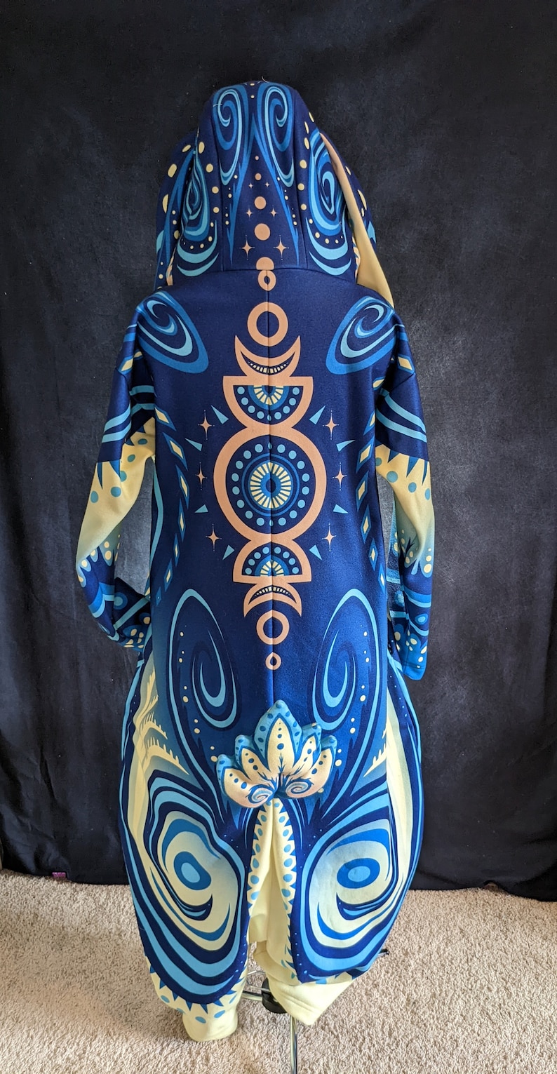 May include: A blue and yellow hooded jacket with a mandala design on the back. The jacket has a long, flowing silhouette and a hood with a drawstring.