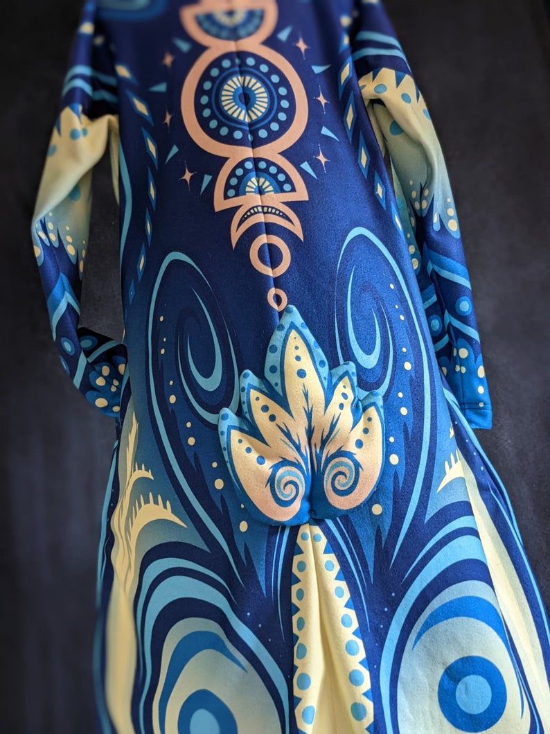 May include: A blue and yellow patterned hooded robe with a geometric design. The robe has a long, flowing silhouette and a hood with a pointed tip.