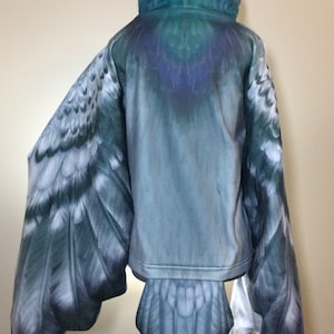 Puede incluir: Una sudadera con capucha azul y gris con un dise&ntilde;o de p&aacute;jaro. La sudadera tiene alas y una cola que parecen las de un p&aacute;jaro.