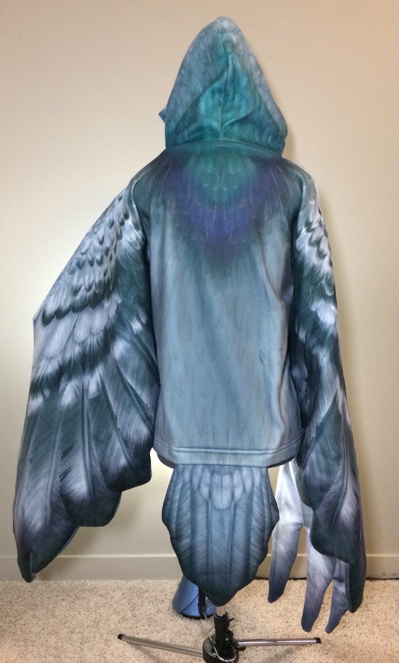 Puede incluir: Una sudadera con capucha azul y gris con un dise&ntilde;o de p&aacute;jaro. La sudadera tiene alas y una cola que parecen las de un p&aacute;jaro.