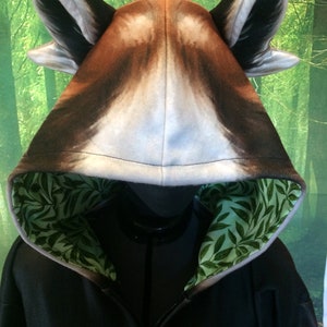 Puede incluir: Sudadera con capucha negra con un dise&ntilde;o de cabeza de lobo en la capucha. La capucha est&aacute; forrada con un patr&oacute;n de hojas verdes.