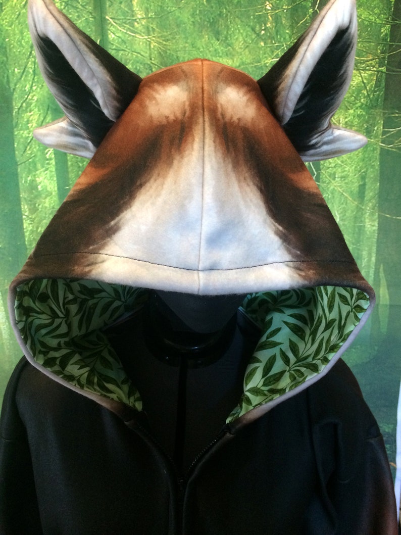 Puede incluir: Sudadera con capucha negra con un dise&ntilde;o de cabeza de lobo en la capucha. La capucha est&aacute; forrada con un patr&oacute;n de hojas verdes.
