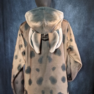 May include: A brown hooded sweatshirt with a black and brown spotted pattern. The hood has two large, light brown ears attached to the back.