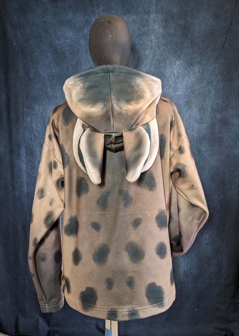 May include: A brown hooded sweatshirt with a black and brown spotted pattern. The hood has two large, light brown ears attached to the back.