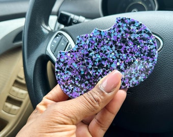 Puede incluir: Dos portavasos redondos para coche con un diseño de purpurina negra, azul y morada.