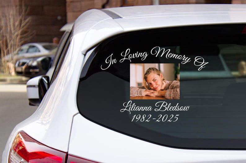 May include: A white car window decal with the text "In Loving Memory Of" and a photo of a woman. The text "Lilianna Bledsoe 1982-2025" is below the photo.
