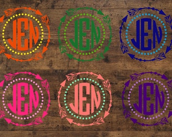 Op de afbeelding: Zes ronde vinyl stickers in verschillende kleuren met een wit monogram "JEN" in het midden. Elke sticker heeft een cirkel van stippen rond het monogram en een ring van pijlen rond de stippen.