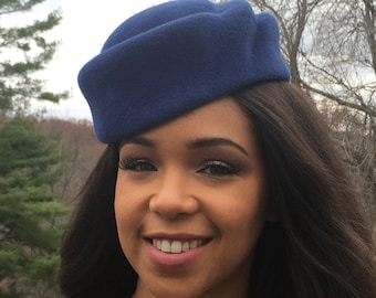 May include: A navy blue hat with a rounded crown and a folded brim. The hat is made of a soft, felt-like material. The hat is worn by a person with long, dark hair.