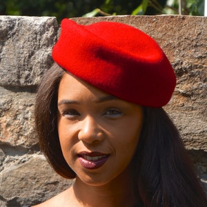 May include: A woman with long dark hair is wearing a red beret. The beret is tilted slightly to the side and covers part of her forehead. She is looking at the camera with a slight smile.