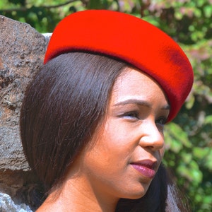 May include: A woman with long dark hair is wearing a red beret. She is looking off to the side.