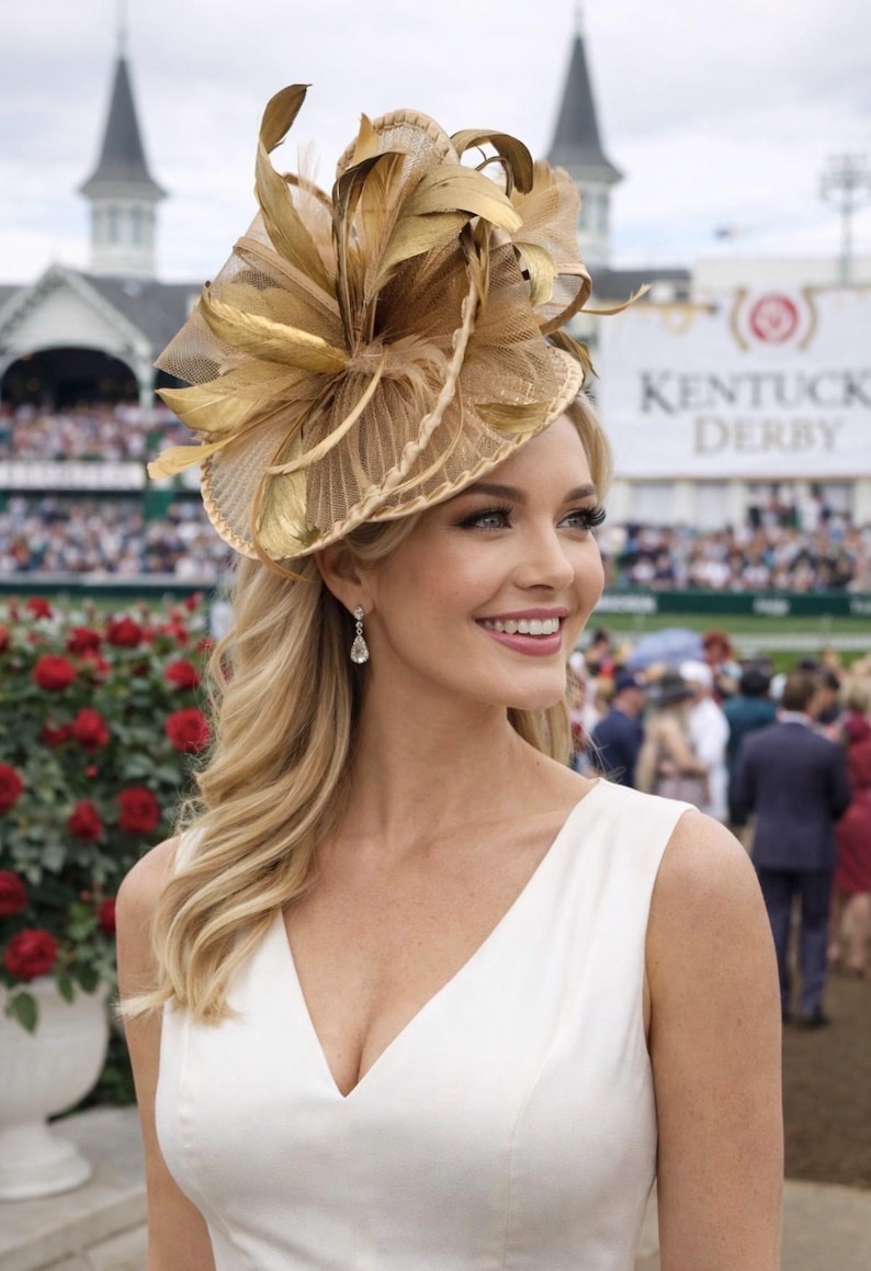 May include: A woman wearing a gold-toned fascinator with feather and net detailing. She is wearing a white dress and diamond earrings. The background includes a crowd and a sign that says "Kentucky Derby".