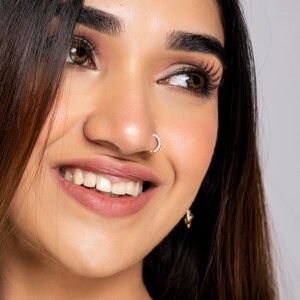 May include: Close-up of a woman's face with long dark hair. She is smiling and has a small diamond nose ring.