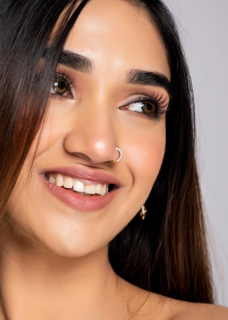 May include: Close-up of a woman's face with long dark hair. She is smiling and has a small diamond nose ring.