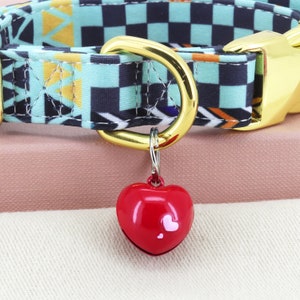 May include: A gold dog collar with a black and turquoise checkered pattern and a red heart-shaped bell charm.
