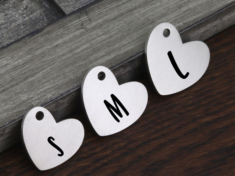 May include: Three silver heart-shaped tags with the letters S, M, and L engraved on them. The tags have a hole at the top for hanging.