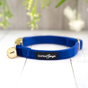 May include: A blue velvet cat collar with a gold bell and a black label that says "Ultra Joys".