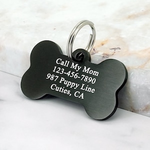 May include: Black bone-shaped dog tag with engraved text: "Call My Mom 123-456-7890 987 Puppy Line Cutie's, CA"