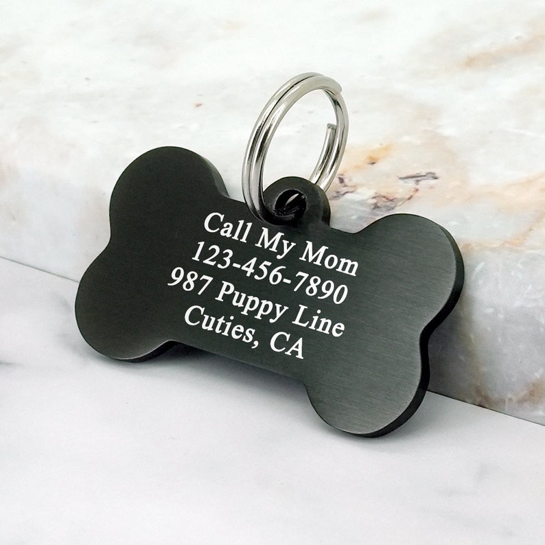 May include: Black bone-shaped dog tag with engraved text: "Call My Mom 123-456-7890 987 Puppy Line Cutie's, CA"