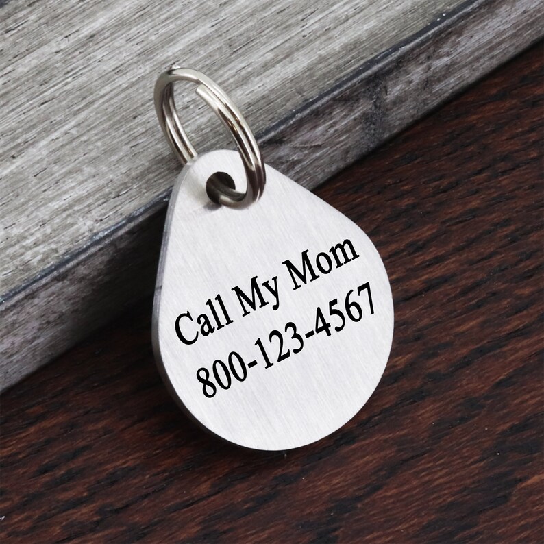 May include: Silver-colored pet ID tag with a teardrop shape and a keyring. The tag is engraved with the text "Call My Mom 800-123-4567".