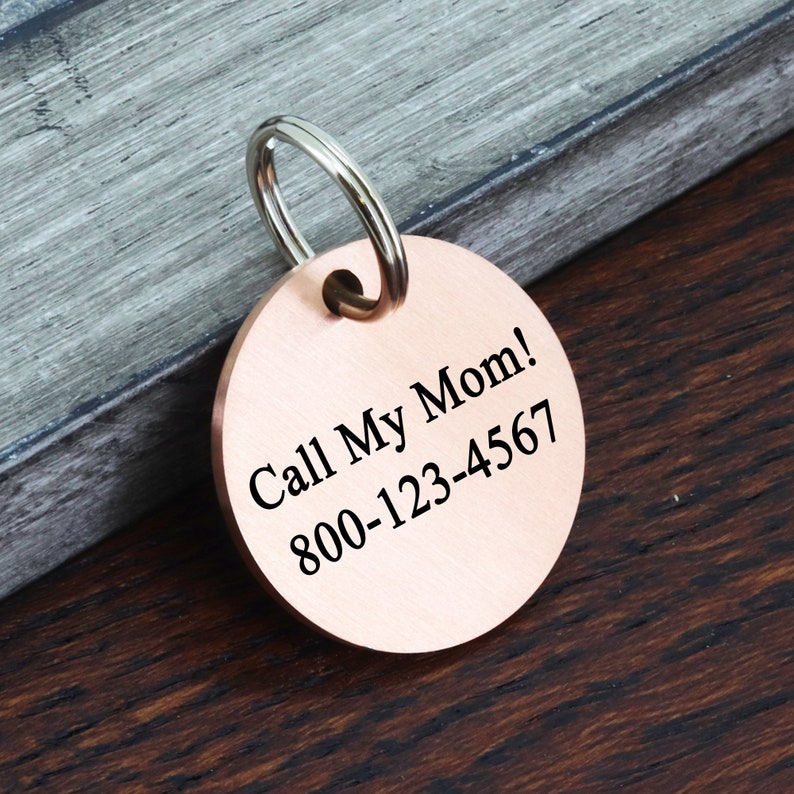 May include: Round copper dog tag with a silver key ring. The tag has the text "Call My Mom! 800-123-4567" engraved on it.