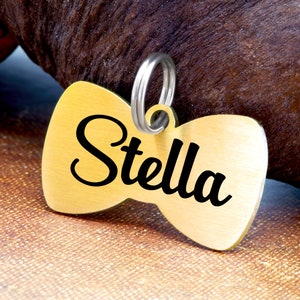 May include: Gold bowtie-shaped dog tag with the name "Stella" engraved in black lettering.