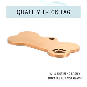 May include: Gold-colored bone-shaped dog tag with a paw print cutout.  "QUALITY THICK TAG" is written in a light blue box above the tag.  "WILL NOT BEND EASILY DURABLE BUT NOT HEAVY" is written below the tag.