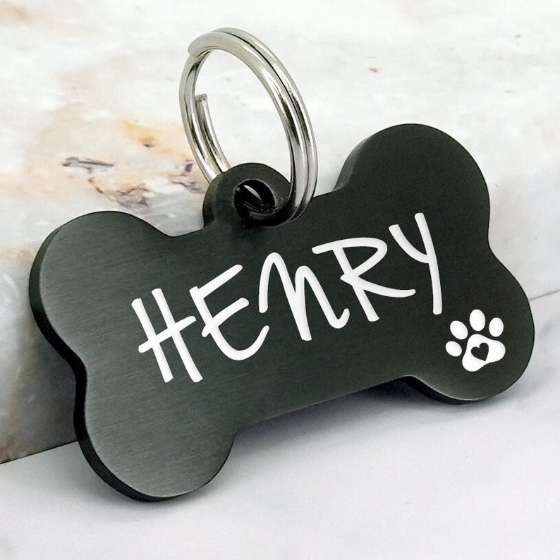 May include: Black bone-shaped dog tag with a silver ring and the name "HENRY" engraved in white lettering. A small paw print is also engraved on the tag.
