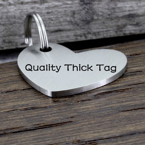 May include: A silver heart-shaped tag with a keyring attached. The tag is engraved with the text "Quality Thick Tag".