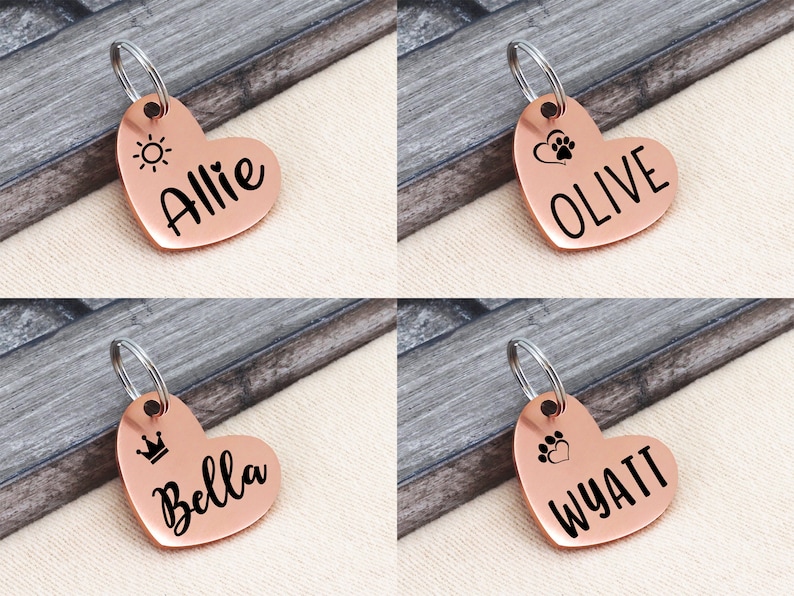May include: Four copper heart-shaped dog tags with different engravings. The tags feature a sun, paw prints, a crown, and a heart. The names Allie, Olive, Bella, and Wyatt are engraved on the tags.