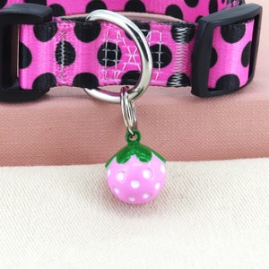 May include: Pink and black polka dot dog collar with a silver D-ring and a pink and white strawberry charm.