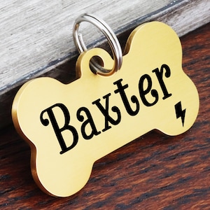 May include: Gold bone-shaped dog tag with a black engraved lightning bolt and the name "Baxter".