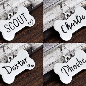 May include: Four silver bone-shaped dog tags with engraved names: Scout, Charlie, Dexter, and Phoebe. Each tag has a small design, such as a heart, paw print, or flower.