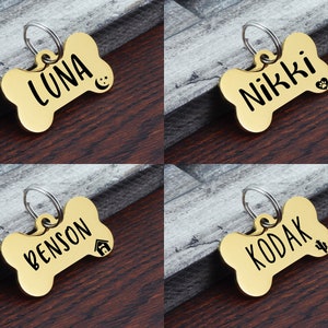 May include: Four gold bone-shaped dog tags with engraved names and small icons. The names are "Luna", "Nikki", "Benson", and "Kodak".