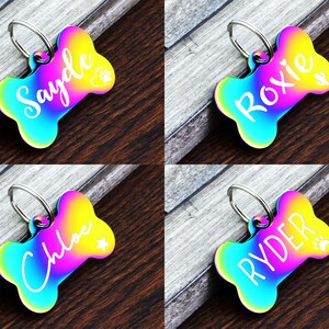 May include: Four rainbow iridescent dog bone shaped tags with personalized names. The names are Sayde, Roxie, Chloe, and Ryder. Each tag has a small paw print or star design.
