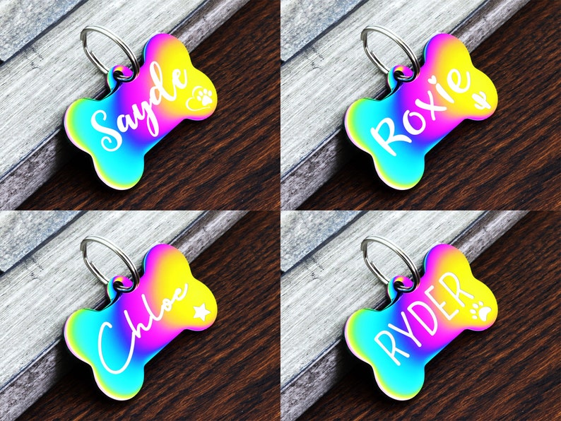 May include: Four rainbow iridescent dog bone shaped tags with personalized names. The names are Sayde, Roxie, Chloe, and Ryder. Each tag has a small paw print or star design.