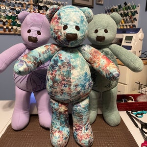 May include: Three handmade teddy bears in a row. The central bear has a floral pattern, while the others are solid lavender and mint green. Each bear has brown felt features and is approximately 24 inches tall.