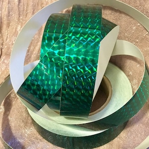 Puede incluir: Rollos de cinta holográfica verde iridiscente. La cinta tiene un patrón de diamante y es reflectante.