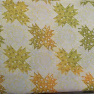 May include: A white fabric with a repeating pattern of yellow and green star-shaped designs. The stars are filled with small white flowers.