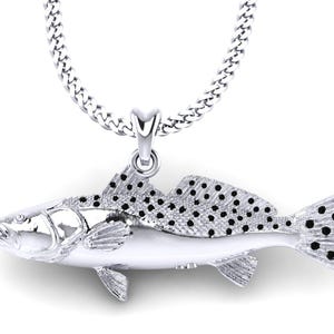 以下が含まれることがあります： 詳細な斑点のある魚のペンダントが付いたシルバーネックレス。この魚は人気のある釣り魚であり、釣り人へのプレゼントに最適です。