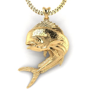 May include: A gold-colored pendant in the shape of a dolphin, with a detailed textured surface. The pendant is attached to a gold chain.