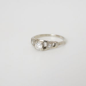 May include: A silver engagement ring with a single round diamond and smaller diamonds on the band.
