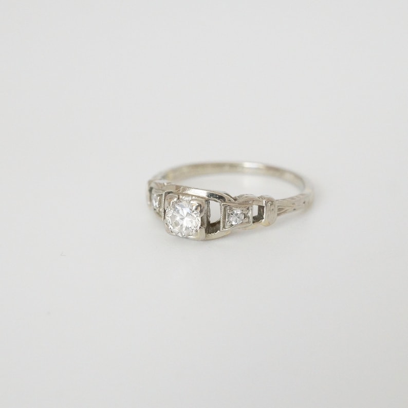 May include: A silver engagement ring with a single round diamond and smaller diamonds on the band.