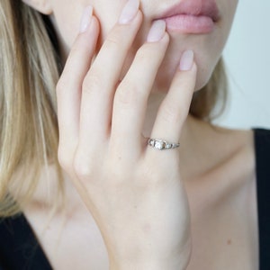May include: A silver ring with a clear square stone set in the centre. The ring is on a woman's finger.