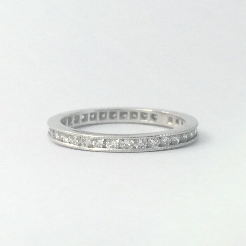 Op de afbeelding: Een dunne zilveren band met een rij kleine diamanten die in een kanaalsetting zijn gezet.