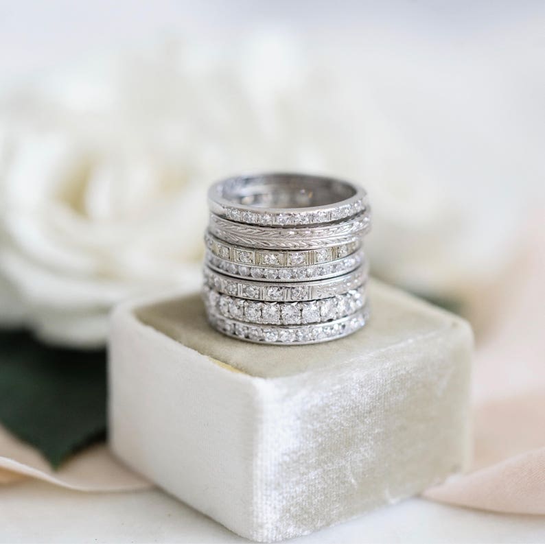 Op de afbeelding: Een stapel zilveren trouwringen met kleine diamanten die in elke ring zijn gezet. De ringen worden gepresenteerd op een witte fluwelen doos.