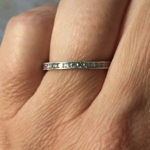 Op de afbeelding: Een dunne zilveren band met een rij kleine diamanten die in een kanaalsetting zijn gezet.