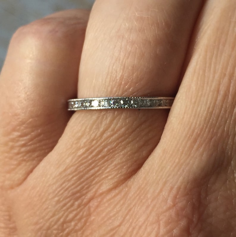 Op de afbeelding: Een dunne zilveren band met een rij kleine diamanten die in een kanaalsetting zijn gezet.