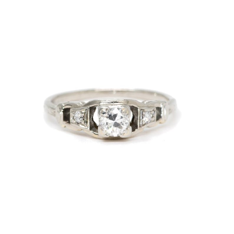 May include: A silver engagement ring with a single round diamond in the centre and smaller diamonds on each side.