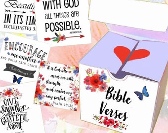 Könnte beinhalten: Eine weiße Box mit einem roten Herzen und den Worten "Bible Verses" darauf gedruckt. Die Box ist geöffnet und enthält 20 kleine Karten mit Bibelversen darauf gedruckt. Die Karten haben Blumenmuster und Schmetterlinge.