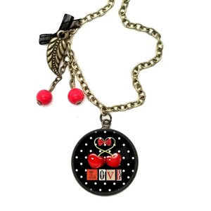 May include: A black and white polka dot necklace with a red cherry charm and the word "LOVE" in red and white letters. The necklace has a gold chain and two red cherry charms hanging from it.